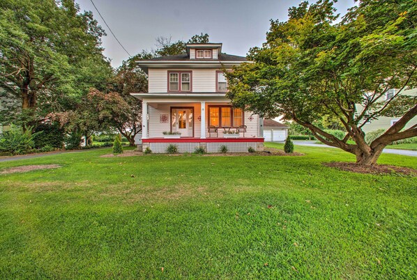 A two-story house with a front porch, a small garden, and a large tree in the front yard. - Whimsical Lancaster Home - 4 Mi to Sight & Sound (Lancaster)