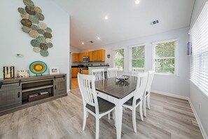 A modern kitchen with wooden cabinets, a dining area with white chairs, and a decorative wall art piece.