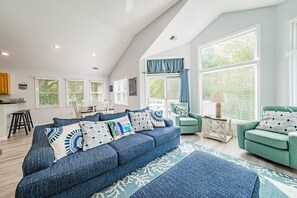 Una sala de estar amplia con techos altos, un sofá azul, un sillón verde y un comedor con mesa y sillas blancas.