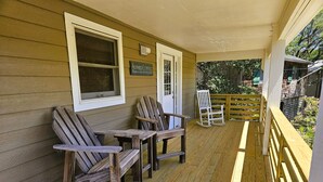 Une véranda en bois avec des fauteuils Adirondack, une chaise berçante et une terrasse en bois.