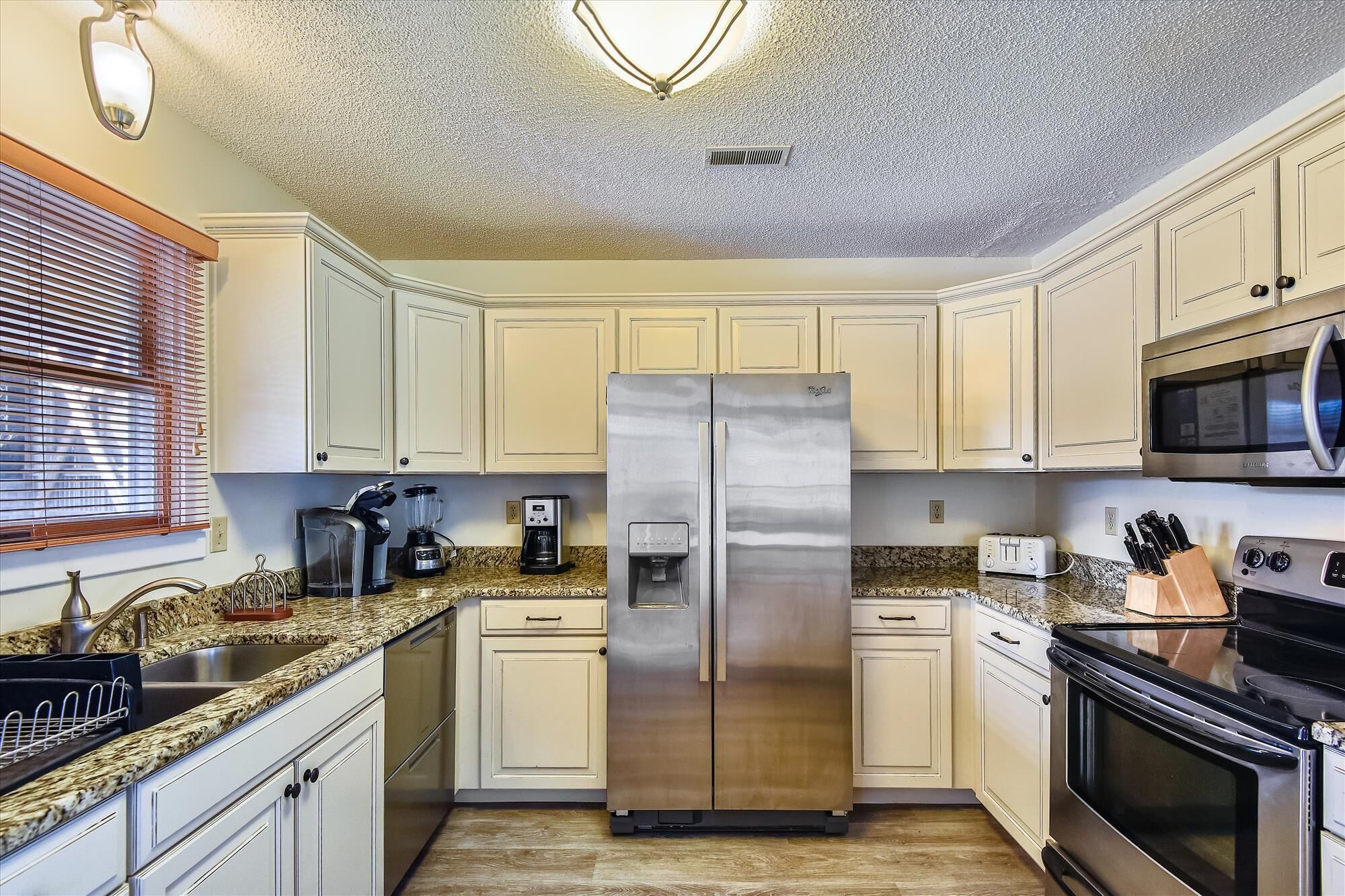A kitchen with white cabinets, a stainless steel refrigerator, a microwave, a toaster, and a sink.