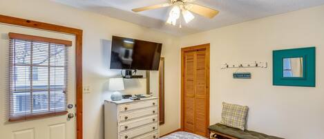 A bedroom with a bed, dresser, television, ceiling fan, and a bench.