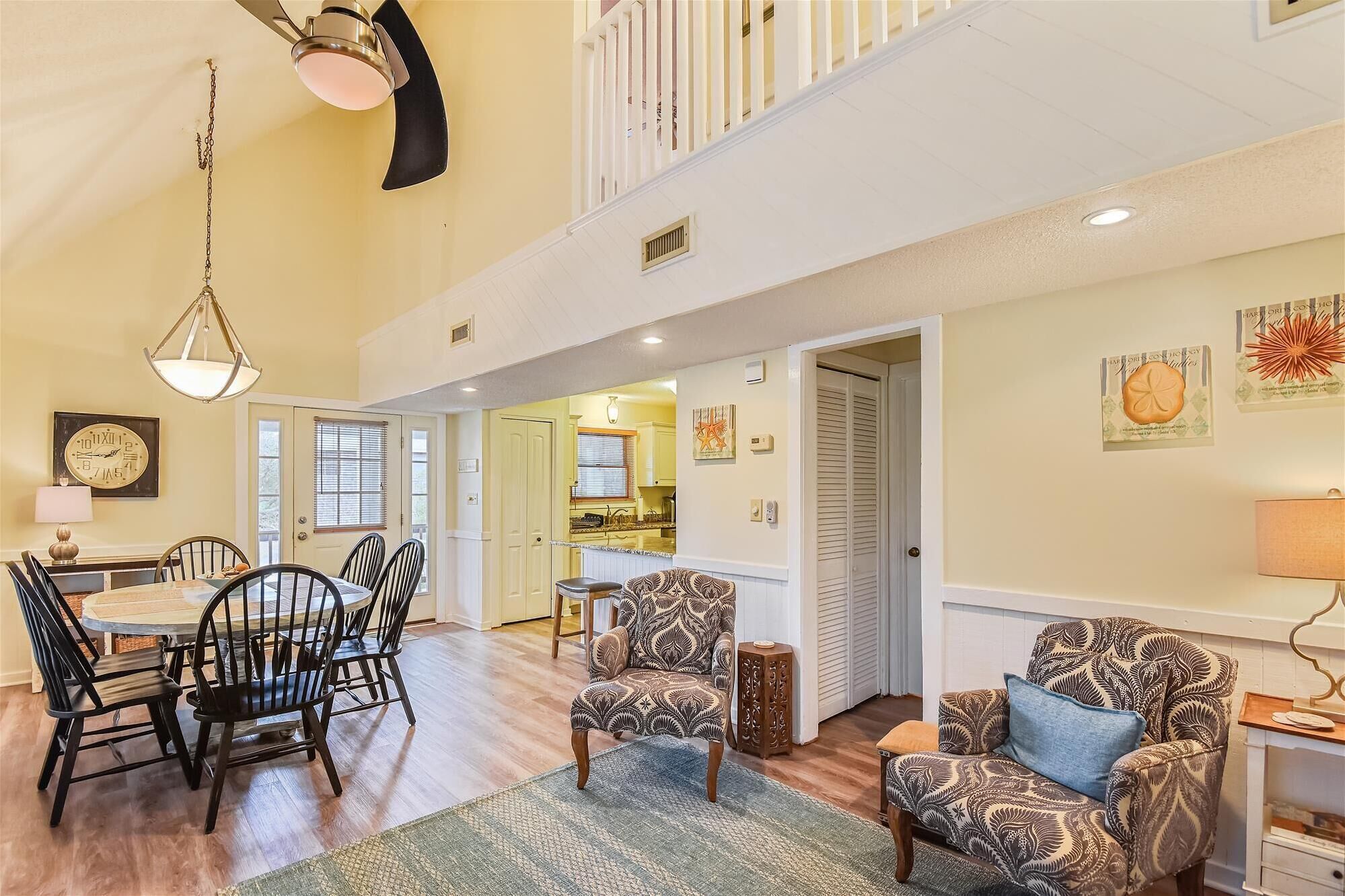 A spacious living area with a dining table and chairs, a patterned armchair, and a ceiling fan.