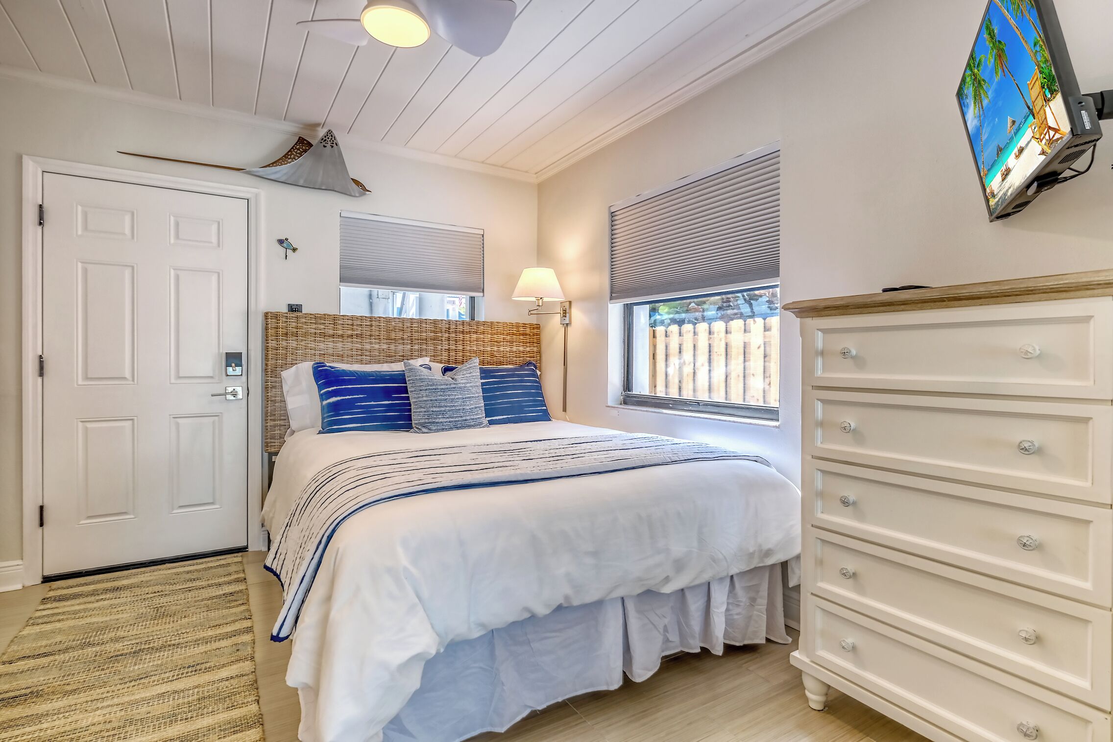 A bedroom with a bed, a dresser, a lamp, a TV, and a window with blinds.