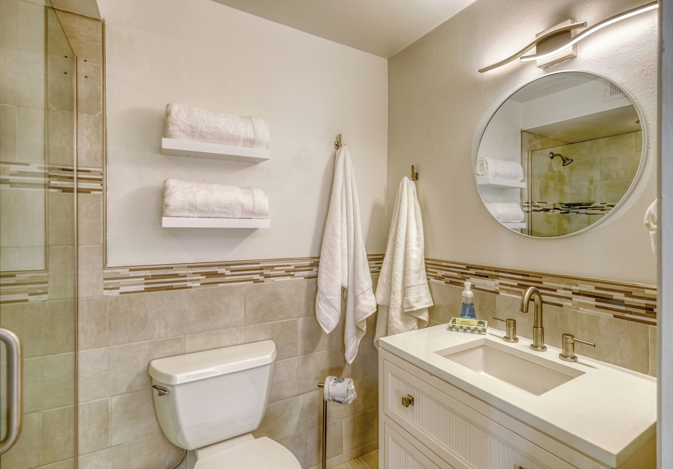 A modern bathroom with a toilet, sink, and mirror. There are towels on the wall and a shower area.