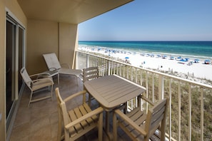 A balcony with a table and chairs, overlooking a beach with umbrellas and people.