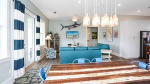 A dining area with a wooden table and blue chairs, a teal sofa, and a ceiling fan. - Directly Next to Community Pool! Beach view! ~Fried Green Tomatoes (Cape San Blas)