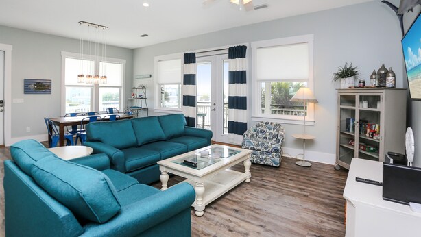 A spacious living room with a sectional sofa, a glass coffee table, and a dining area with a table and chairs. - Directly Next to Community Pool! Beach view! ~Fried Green Tomatoes (Cape San Blas)