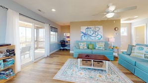 A spacious living room with a blue sofa, a coffee table, and a ceiling fan. - Summer Paws | 3BR 4x4 OBX | Hot Tub | Pets | 4 night stay available for fall (Carova)