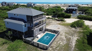 A multi-story building with a rooftop pool, surrounded by vegetation and a beach.