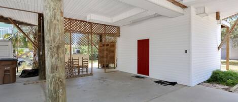 A covered outdoor area with a concrete floor, a wooden table and chairs, a red door, and a lattice fence.