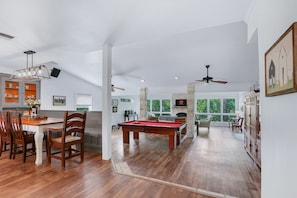 A spacious room with a pool table, wooden chairs, a dining table, and a fireplace.