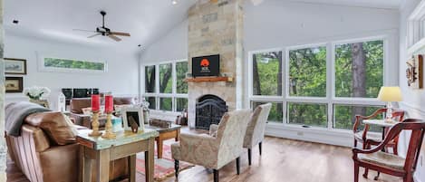 Una sala de estar amplia con chimenea, ventanas grandes y ventilador de techo.
