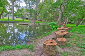 A serene park with a pond, surrounded by trees and a row of wooden stumps.