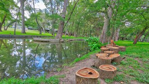 A serene park with a pond, surrounded by trees and a row of wooden stumps. - On the Creek, Sleeps 10, Close to Town - Perfect Wimberley Escape (Wimberley)