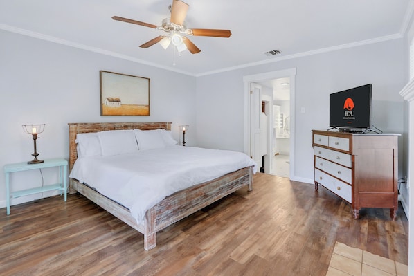 A bedroom with a wooden bed, a ceiling fan, a television, and a dresser.