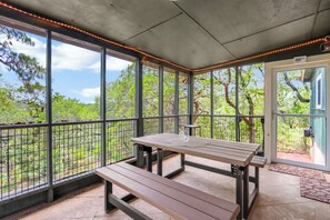 Un porche cubierto con una mesa, un banco, ventanas amplias y vistas al follaje.