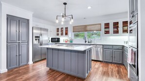 A modern kitchen with grey cabinetry, a central island, stainless steel appliances, and a large window. - On the Creek, Sleeps 10, Close to Town - Perfect Wimberley Escape (Wimberley)
