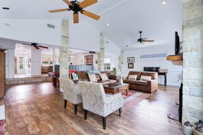 A spacious living room with a wooden floor, a brown leather sofa, patterned armchairs, and a coffee table.