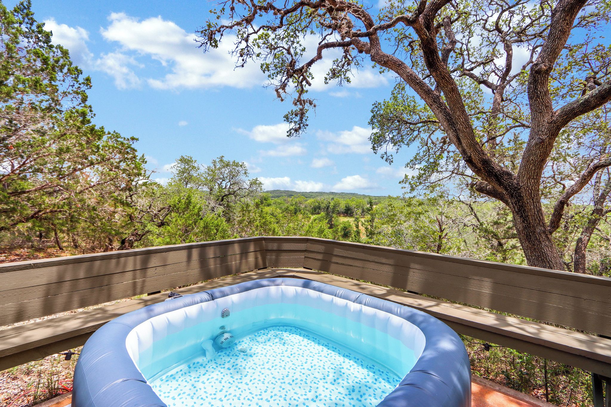 Una piscina inflable sobre una terraza de madera con vistas a árboles y colinas.
