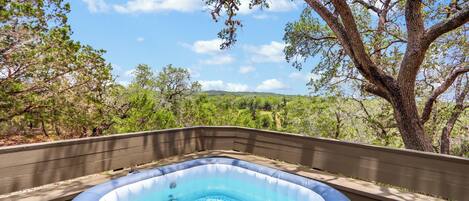 Una piscina inflable sobre una terraza de madera con vistas a árboles y colinas.