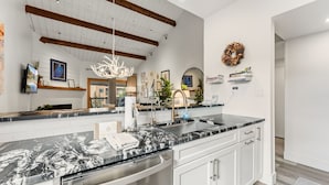 A modern kitchen with marble countertops, stainless steel appliances, and a high ceiling with exposed beams. - Luxury Ski-In Condo | 2023 Remodel | Walk to Peak 9 Lift and Mountain Views (Breckenridge)