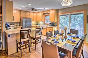 A modern kitchen with wooden cabinets, a stainless steel refrigerator, and a dining area with a table set for four. - Secluded 'Lavinder Laurel Leaf Cottage' Near Creek (Lakemont)