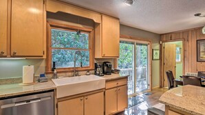 A kitchen with wooden cabinets, a stainless steel dishwasher, a sink, and a window with a view of greenery. - Secluded 'Lavinder Laurel Leaf Cottage' Near Creek (Lakemont)