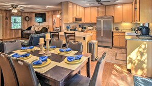 A modern kitchen with wooden cabinets, stainless steel appliances, and a dining area set for six with blue napkins and placemats. - Secluded 'Lavinder Laurel Leaf Cottage' Near Creek (Lakemont)
