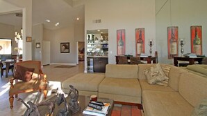 A spacious living room with a large sectional sofa, a coffee table with decorative items, and a kitchen in the background. - Delightful 3 Bed Home with Amazing Views LQ171 LIC#110324 (La Quinta)