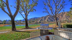 A patio with a grill, a table with a vase, and a view of a golf course and mountains. - Delightful 3 Bed Home with Amazing Views LQ171 LIC#110324 (La Quinta)