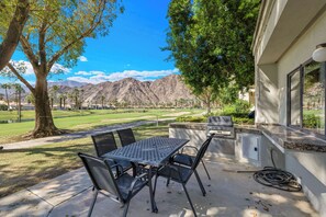 Un patio exterior con mesa y sillas, una parrilla y vistas a un campo de golf y montañas.