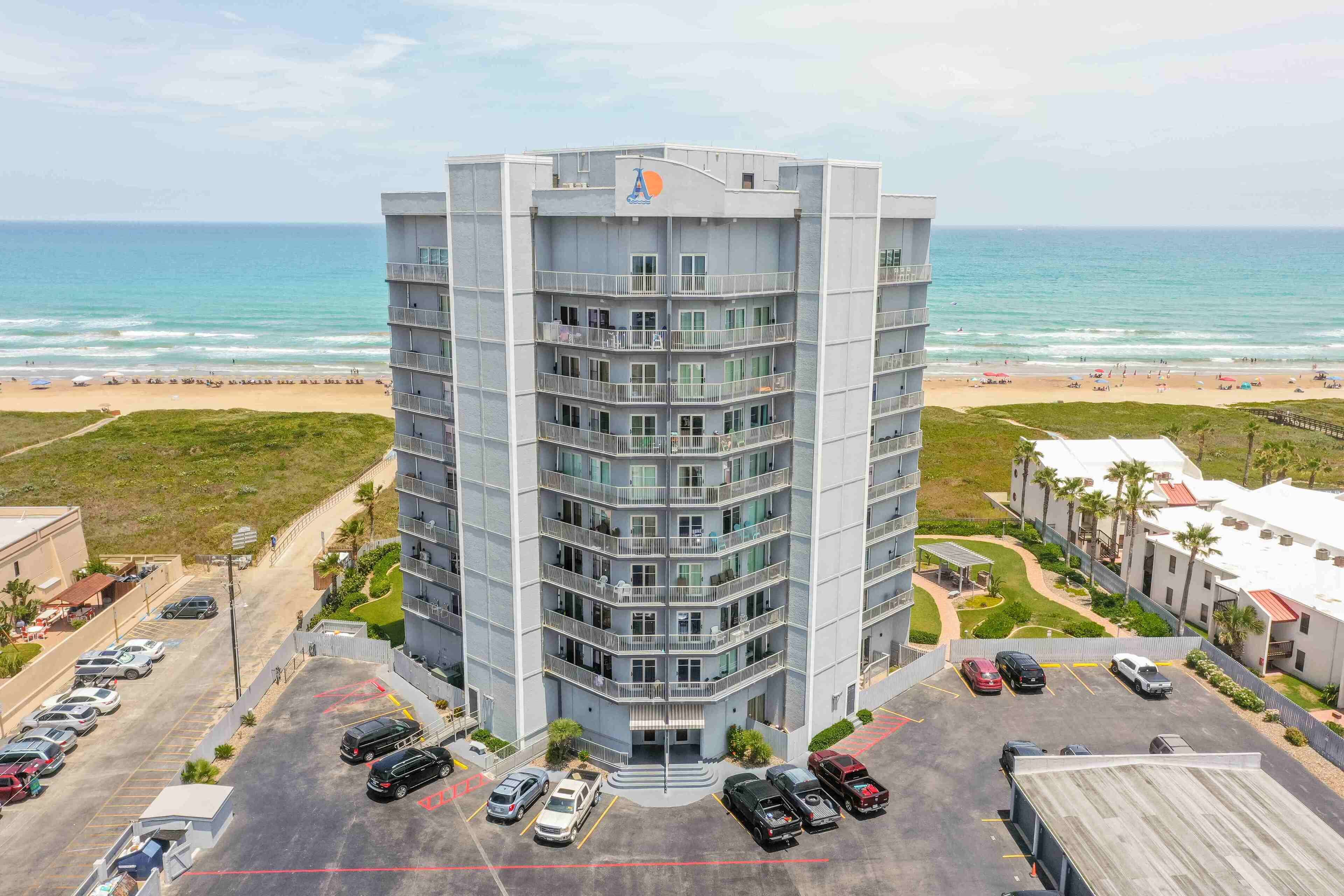 Un hotel de varios pisos con una entrada principal, estacionamiento y vistas a la playa.