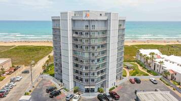 Un hotel de varios pisos con una entrada principal, estacionamiento y vistas a la playa.