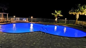 Una piscina nocturna de diseño curvo, rodeada por una terraza empedrada y palmeras.