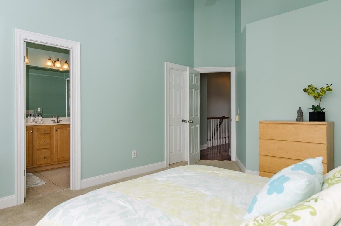 A bedroom with a bed, a dresser, a mirror, and a door leading to a bathroom.