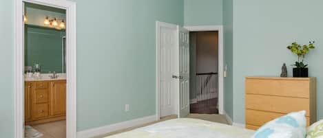 A bedroom with a bed, a dresser, a mirror, and a door leading to a bathroom.