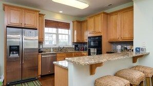 Una cocina con armarios de madera, electrodomésticos de acero inoxidable, encimera de granito y una ventana con persianas.