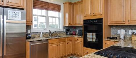 A modern kitchen with wooden cabinets, stainless steel appliances, granite countertops, and a window with blinds.