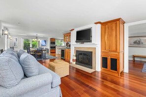 A spacious living room with a fireplace, wooden cabinets, and a television mounted above it.