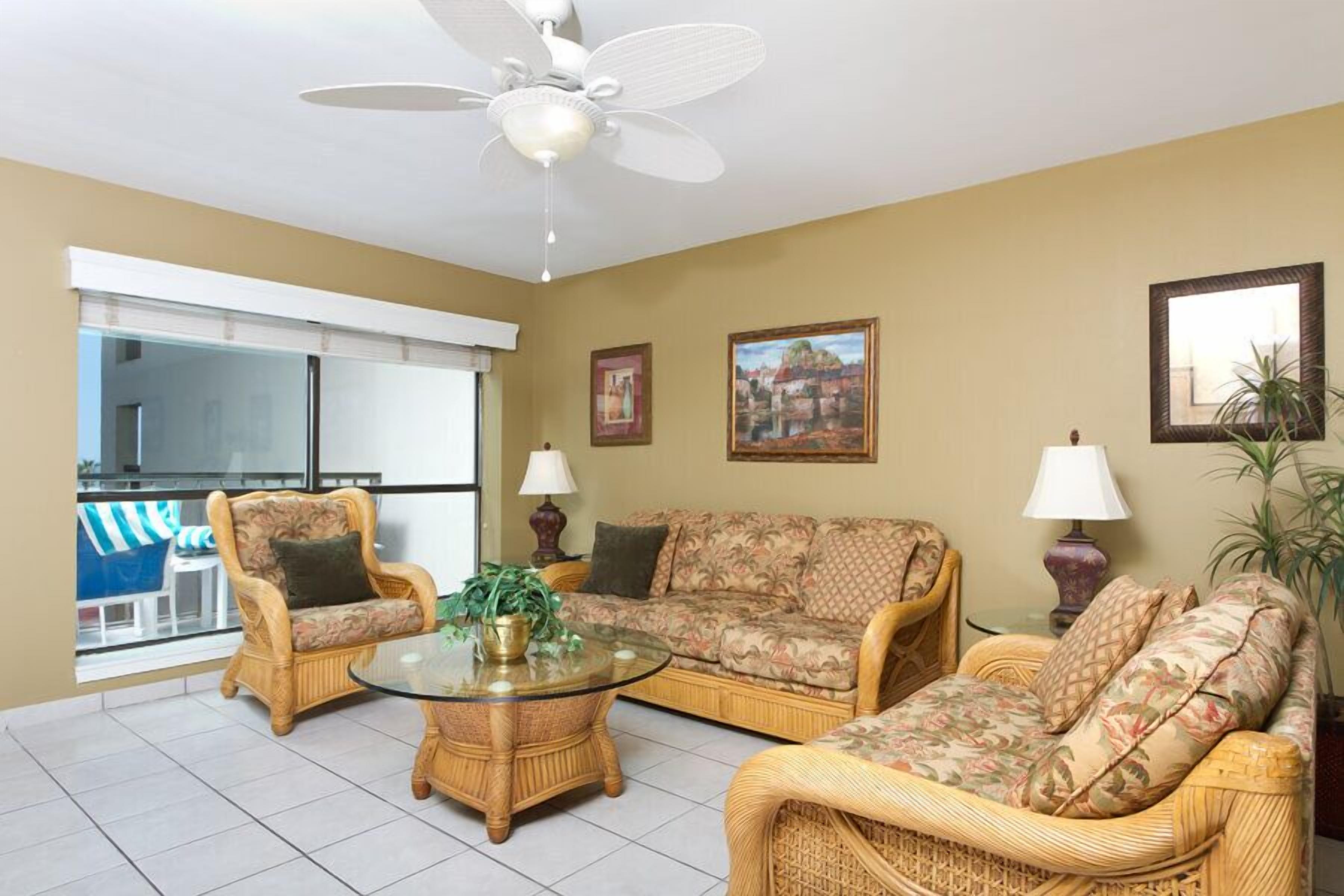 A living room with wicker furniture, a glass coffee table, and a ceiling fan.