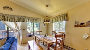 Un comedor acogedor con una mesa de madera, sillas y un banco. Hay un sofá azul y una ventana con cortinas.