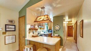 Una cocina con una isla central, taburetes de bar, una lámpara colgante y piso de baldosas de piedra.