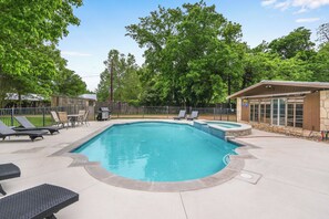 A swimming pool with a stone deck, surrounded by lounge chairs and a covered area.