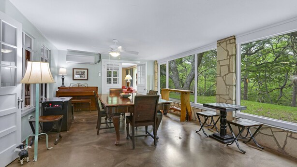 A spacious dining area with a large table and chairs, a piano, and a view of a lush green landscape through large windows.