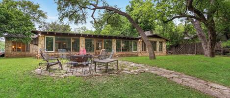 A stone house with a patio, outdoor seating, and a large tree.