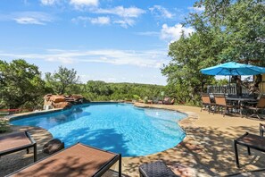 Piscina com cachoeira, rodeada por árvores e mobiliário de exterior.