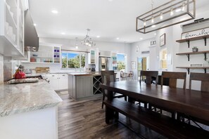 Cozinha moderna com armários brancos, uma ilha central e um espaço de jantar com mesa de madeira e bancos.