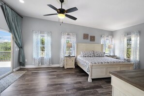 Quarto com cama, mesas de cabeceira, ventilador de teto e janelas amplas com cortinas.