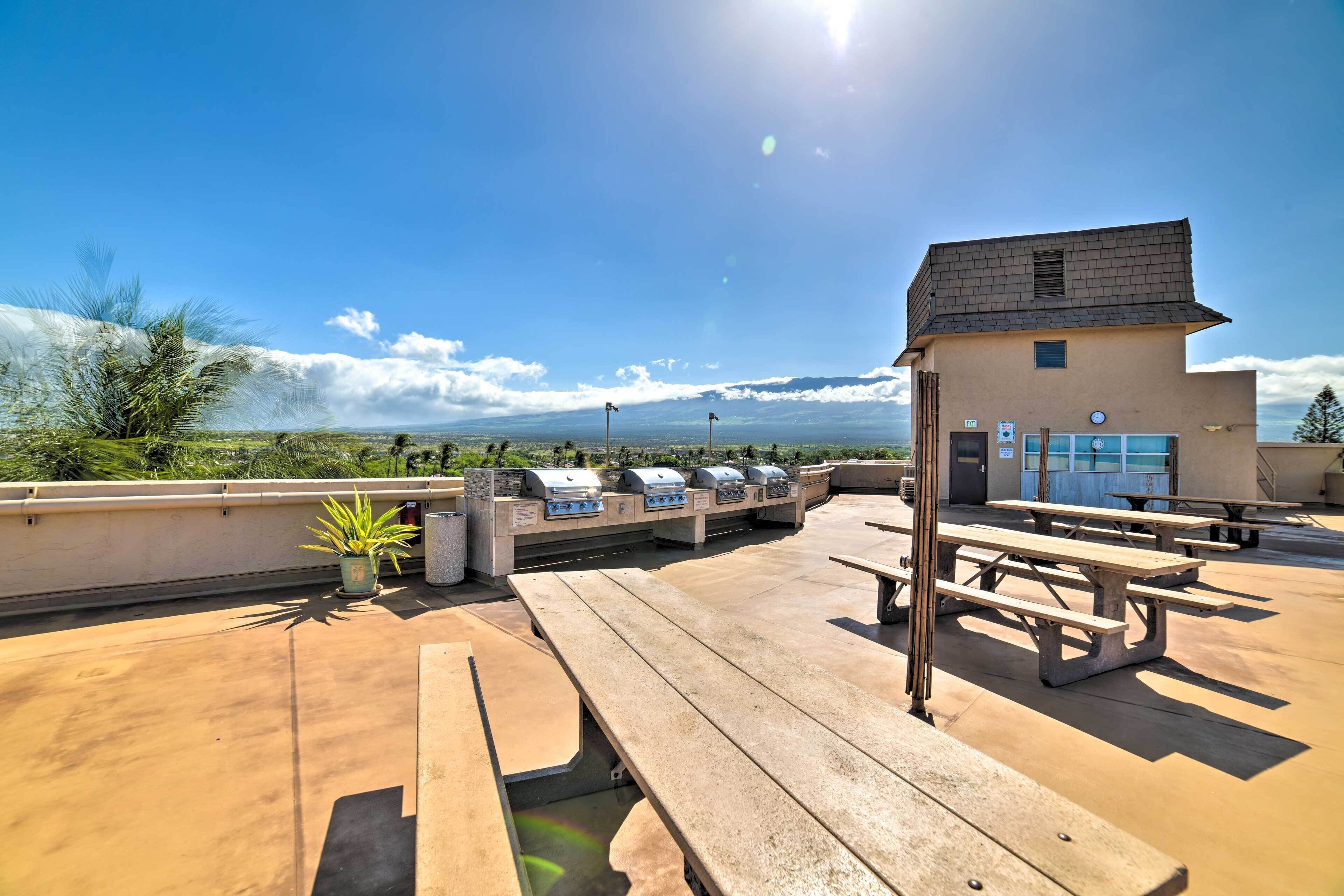 Eine Terrasse im Freien mit Picknicktischen, Grillanlagen und einem kleinen Gebäude.